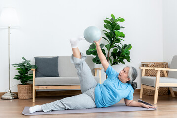 Asian elderly woman doing exercise at home by stretching the leg muscles and using a ball as an...