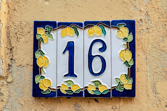 Ceramic background. Italian traditional patterns on tiles, handmade craft painting - numbers for apartments and houses. Number sixteen 16 with lemons.
