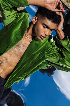 top view of young african american man in green velvet blazer lying on mirror outdoors