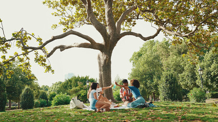 Happy smiling young multinational people at picnic on summer day outdoors. Friends have fun weekend together, relaxing in the park at picnic