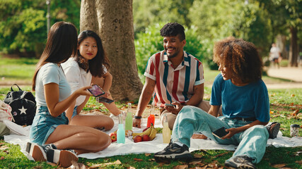 Close-up of young man with curly hair wearing striped shirt sitting in park having picnic on summer day outdoors, talking with friends - obrazy, fototapety, plakaty