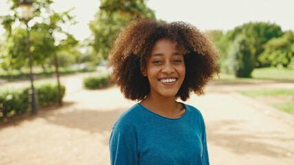Close-up of young smiling woman with curly hair wearing blue t-shirt posing for the camera in the...