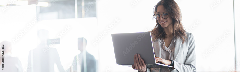 Wall mural Mature smiling businesswoman at office with group of colleagues on background, working on laptop