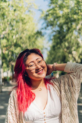 Happy casually dressed Asian young woman with dyed red hair smiling and looking at camera
