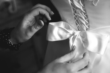 Grayscale close-up shot of hands tying a bow on a wedding dress