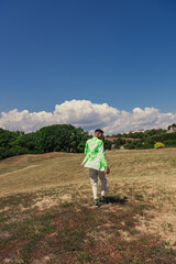 back view of african american man in stylish blazer walking in grassy meadow