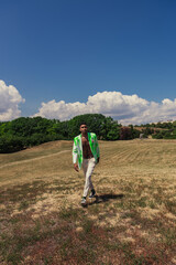 Fototapeta premium full length of stylish african american man walking in field with green trees