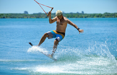 A professional wakeboarder rides on the lake in sunny weather, performing figures