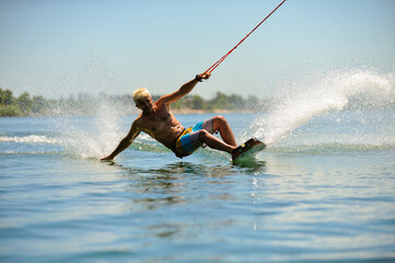 A professional wakeboarder rides on the lake in sunny weather, performing figures
