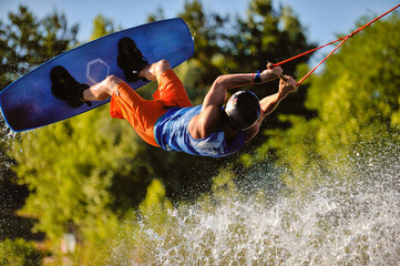 Professional wakeboarder jumping over the water against the sky and trees