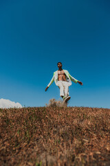 african american man in trendy summer outfit posing in field under blue sky