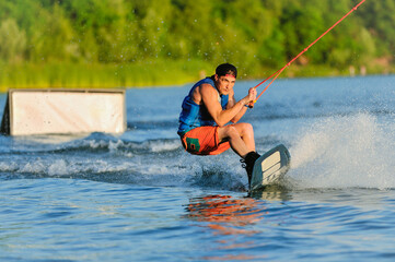 A professional wakeboarder rides on the lake in sunny weather, performing figures