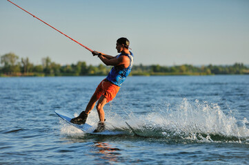 A professional wakeboarder rides on the lake in sunny weather, performing figures