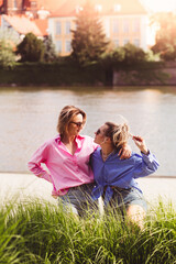Fototapeta premium Portrait of two young beautiful smiling hipster female in trendy summer color clothes. carefree women posing on river background. Positive models having fun, hugging