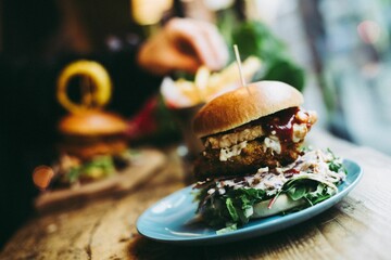 Tasty vegan burger sandwich in blue dish on wooden table