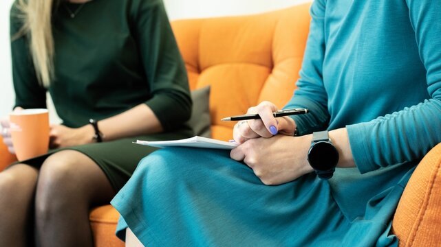 Office interview between two ladies sitting on orange sofa and discussing