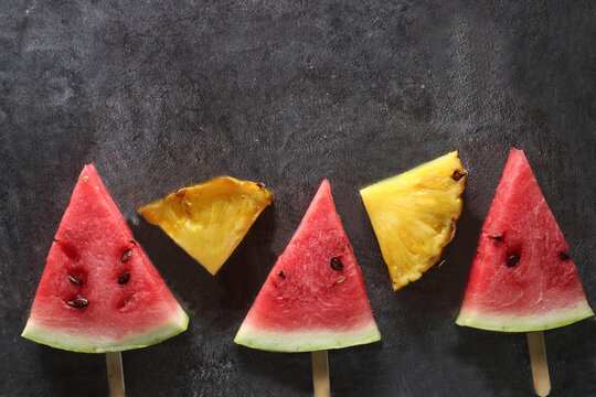 slices of water-melon and pineapple on popsickle stick on gray background flat lay