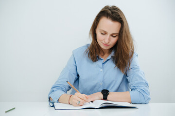 Diligent smirking business woman in blue dress shirt writing in a journal, looking down at it.