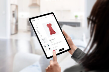 Woman buys a dress online with tablet concept. Modern e-commerce clothing website. Living room in...