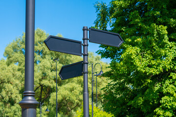 Blank signs with directions in the park. Black arrows against the sky and green trees.
