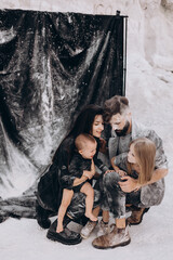 young family with 2 kids dressed in black clothes posing for a photo during a stylized photo shoot in a natural white location, fun, stylish and charismatic. Family with two daughters