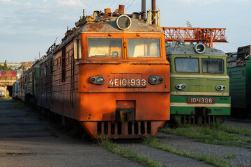 Abandoned decommissioned orange and green soviet locomotives stand on overgrown railway in stock near station in Tbilisi, Georgia. Old railway machines and engineering left outdoor in city
