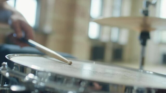 Close up dutch angle shot of drumsticks hitting snare drum as unrecognizable man playing music in studio