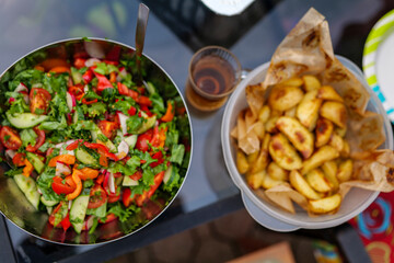 selective focus. Fresh cut spring vegetables mixed salad, slices of oven-cooked potatoes, and a glass of tea on the backyard table. Summer food compilation High-quality photo