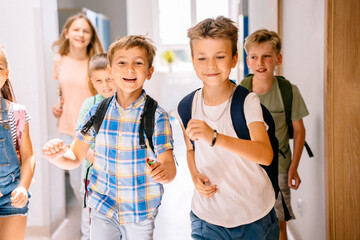 School kids enjoy free time running to camera in elementary school hallway.