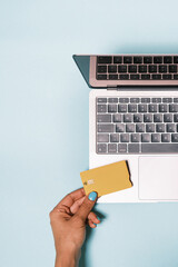 Top view of anonymous hand holding a bank credit card while making an online payment with a computer