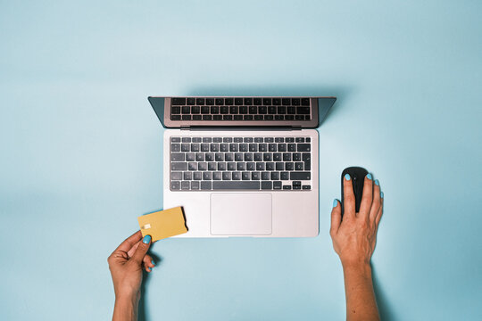 Top view of anonymous hand browsing on the computer with pc mouse and holding a bank credit card while making an online payment