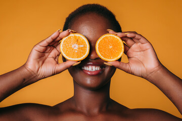 Portrait of african american woman holding halves of orange on her eyes isolated on orange...