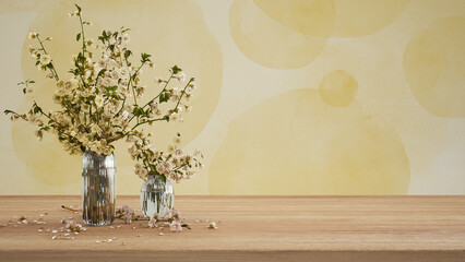 Wooden table, desk or shelf close up. Branches of cherry blossoms in glass vase. Plaster painted wall in yellow tones with copy space, template, mock up, spring concept