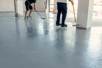 Construction workers applying grey epoxy resin in an industrial hall
