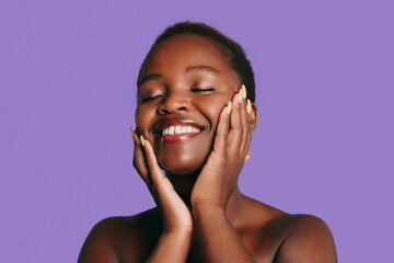 Happy African-American woman model touching face skin care on purple background. Ethnic natural...