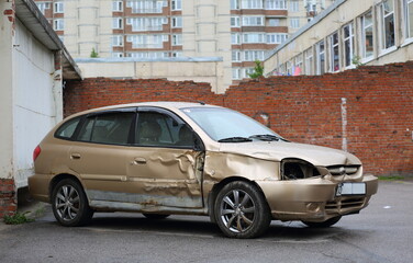 A broken light brown car in the yard near the wall, Podvoysky Street, St. Petersburg, Russia, August 2022