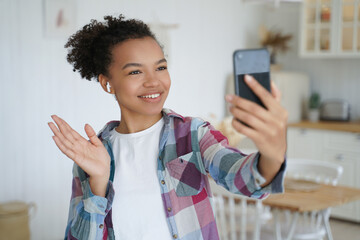Young mixed race girl blogger holds smartphone use video call, greeting followers in social network
