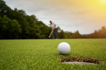 Golfer putting ball on the green golf, lens flare on sun set evening time.