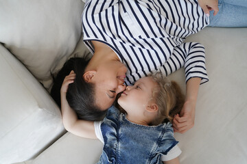 Loving mother lying on couch touching nose face with kid daughter. Happy motherhood, family bond