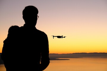 Silhouettes of two people piloting the drone at sunset