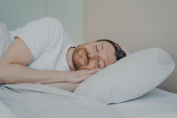 Fototapeta na wymiar Close up view photo of bearded young male fall asleep in his bed