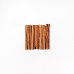 Flat lay arrangement of cinnamon sticks stacked in a square in the center. A minimalistic concept of spices for coffee and drinks, as well as baking. Top view.