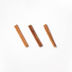 Arrangement of three cinnamon sticks arranged diagonally in the center in a flat lay. Minimalistic culinary concept in oriental style from spices for cooking and baking. Top view in square orientation