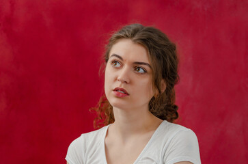 Portrait of a pensive charming young woman. Long curly dark hair. Looks to the side. Red background.