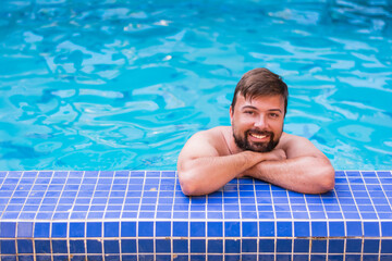 Portrait of a man 30 years old smiling positive naked in a blue pool resting on a weekend or vacation in the summer on a sunny day. Concept: rest in hotels by the pool 