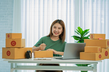 Portrait of a small business startup, SME owner, young Asian entrepreneur, working, unboxing, checking orders online. To prepare to pack parcel delivery boxes for sale to SME customers online business