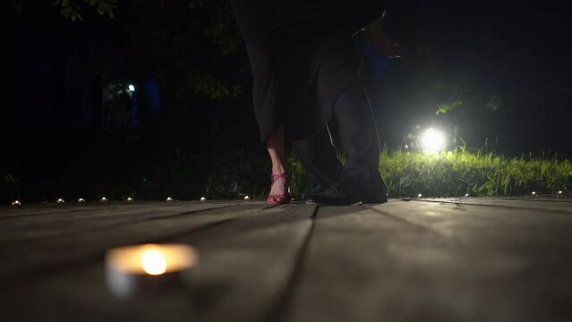 Closeup dancers legs performing latin dance on wooden support. Unknown couple feet dancing tango in dark background. Backlight, slow motion