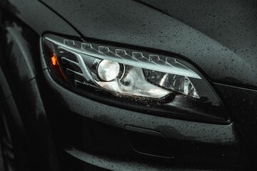 Closeup shot of the front light of a modern car with water droplets on it - Powered by Adobe