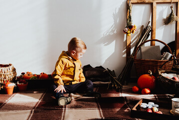 Cool trendy hipster boy 2 years old wears yellow jacket posing at the decorated photozone of autumn decor with beautiful bright autumn leaves.