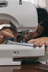 Vertical shot of middle-aged woman with curly hair basting her dress on automatic sewing machine....
